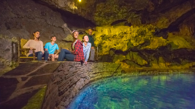 Des visiteurs assis aux abords d'eaux thermales turquoise dans une grotte