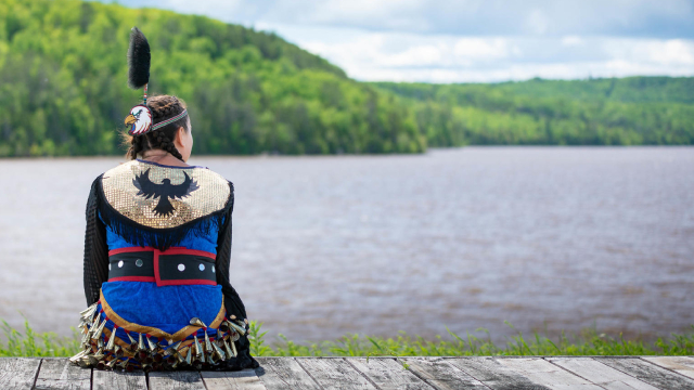 Une personne en tenue traditionnelle autochtone observe un lac