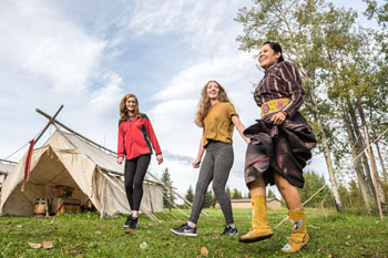 Au camp Métis, deux jeunes femmes dansent une gigue Métis en suivant les pas d'une femme autochtone. Lieu historique national Rocky Mountain House.