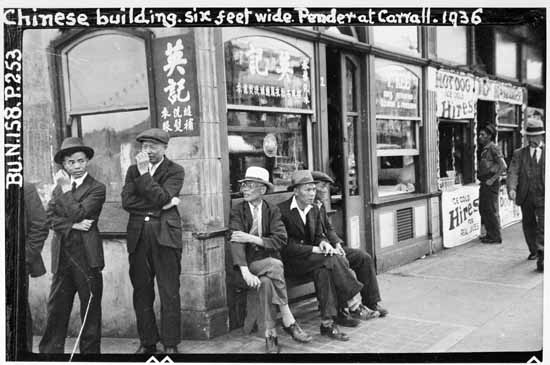Photo en noir et blanc d'un group d'hommes debout et assis sur le coin d'un immeuble