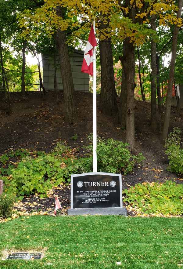 Une pierre de sépulture entourée d'arbres et un drapeau du Canada