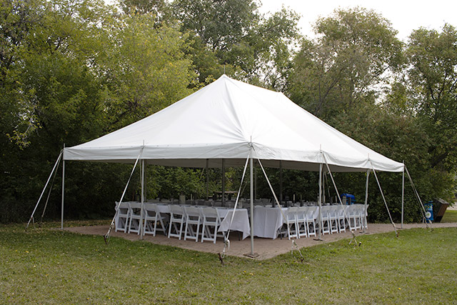 Des chaises sont disposées autour de tables rectangulaires sous une tente au lieu historique national de la Maison-Riel.