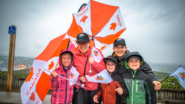 une famille de cinq personnes tenant des drapeaux canadiens et des parapluies du Canada