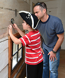Un homme et un enfant examinent les images laissées sur le mur du blockhaus au fort Edward.