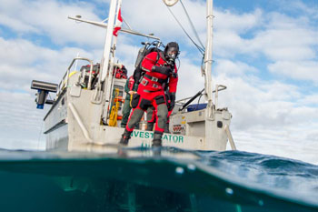 Plongeur en combinaisons isothermique à la poupe d'un bateau; La moitié de l'image est sous l'eau.