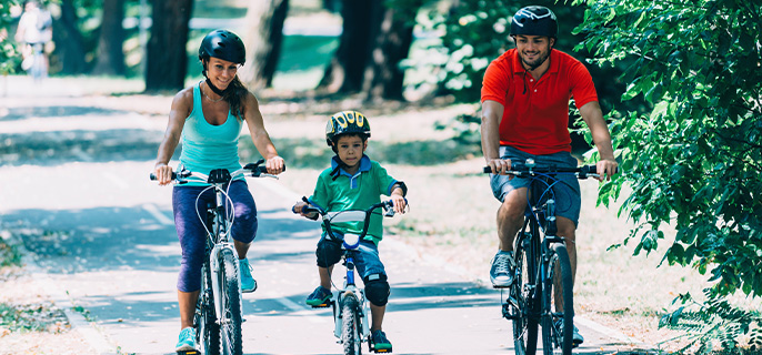 Une maman, un papa et leur enfant circulent à vélo sur une piste cyclable lors d'une belle journée d'été.
