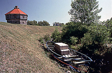Vue du canal rigolet, un endiguement de pierres parallèle au rivage, une représentation d'un bateau canadien et d'un batelier rappellent le paysage d'époque.