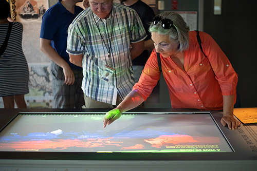 Des visiteurs interagissent avec un panneau d'interprétation de l'exposition