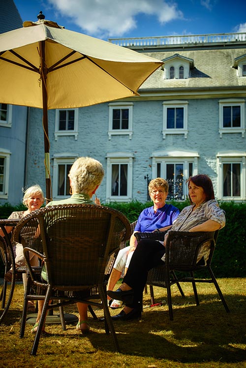 Des dames discutent sous un parasol dans la cour arrière du Manoir Papineau