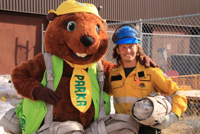 Parka, la mascotte de Parcs Canada, pose avec un membre de l’équipe des pompiers. Tous deux tiennent un tuyau d’incendie enroulé, communément appelé « melon ».