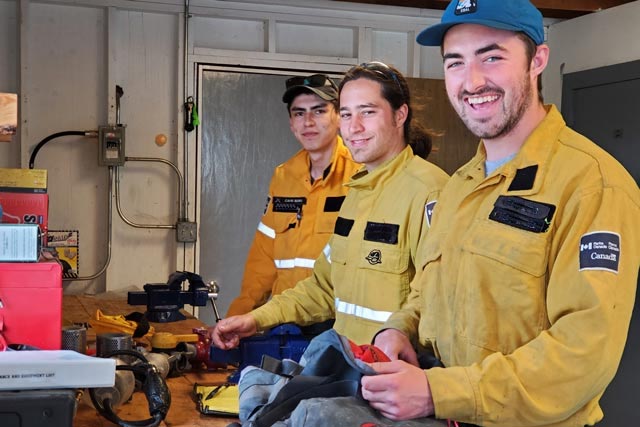 Trois membres de l’équipe de pompiers sourient alors qu’ils préparent leur équipement de terrain pour leur journée dans le parc national Wood Buffalo.