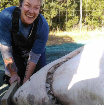 Une femme se tenant à côté d’un requin mort.