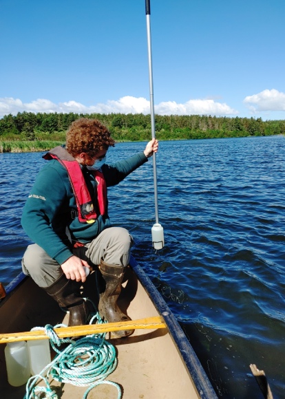 Un employé de Parcs Canada est assis dans un canoë et utilise une longue perche pour prélever des échantillons d’eau.