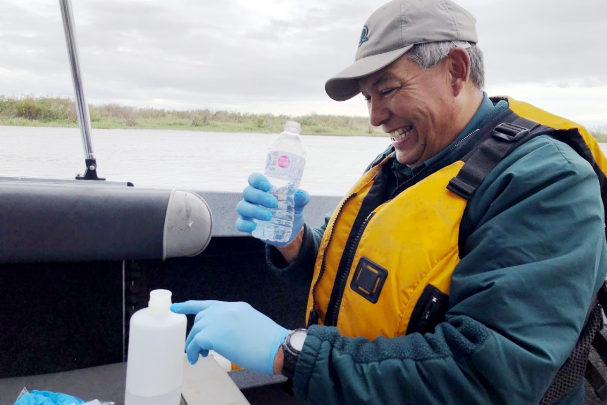 Un membre du personnel de Parcs Canada aux mains gantées prélève des échantillons d'eau dans un pot transparent pour de l'ADN environnemental.