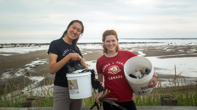 Deux personnes souriantes participant à un nettoyage montrent fièrement les déchets qu'elles ont accumulées dans des seaux de plastique.
