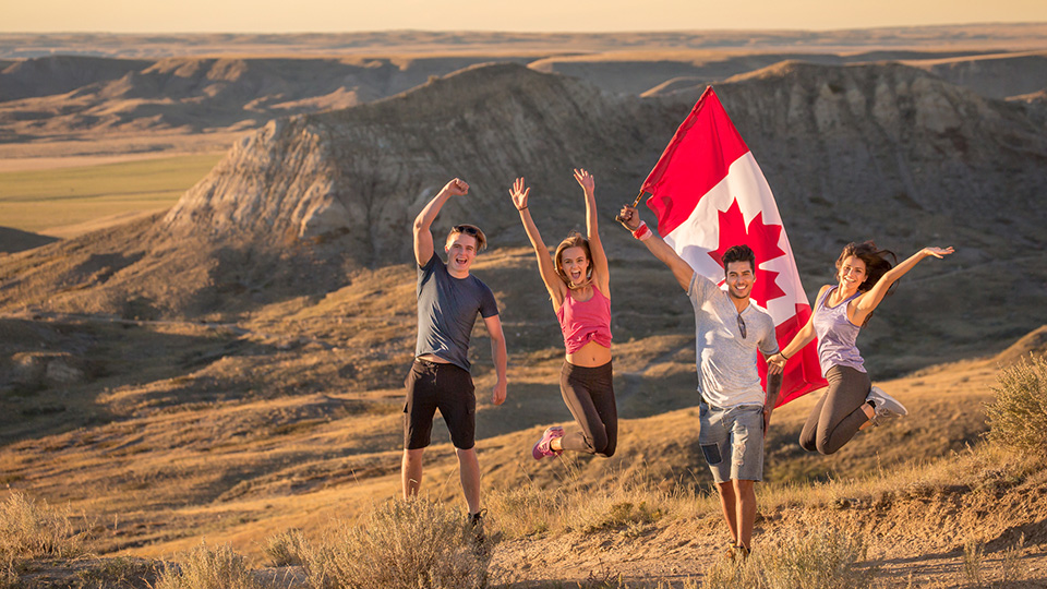 Quatre jeunes adultes célèbrent le Canada à l'aide d'un drapeau canadien lors d'une randonnée au parc national des Prairies.