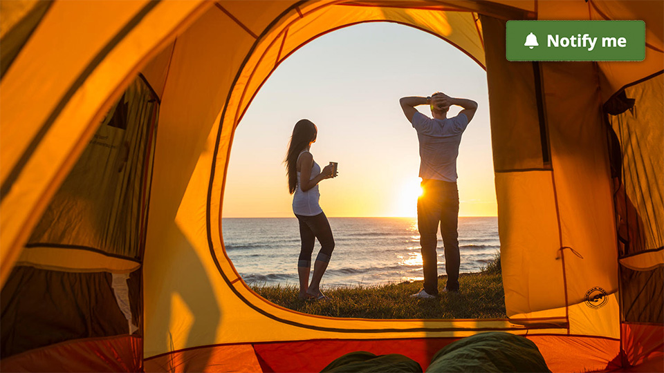 A young couple watches the sunrise outside their tent at Cavendish Campground, with the overlay of a notify me button.