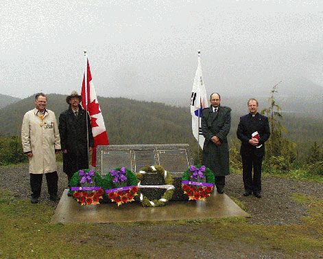 Des officiers se tiennent sur la colline Radar près de la plaque commémorative, entourés de drapeaux et de couronnes