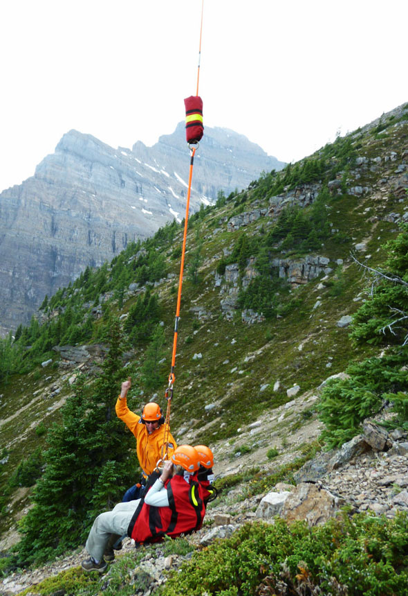 Un spécialiste de la Sécurité des visiteurs fait signe à l'hélicoptère de soulever deux grimpeurs installés dans des baudriers.