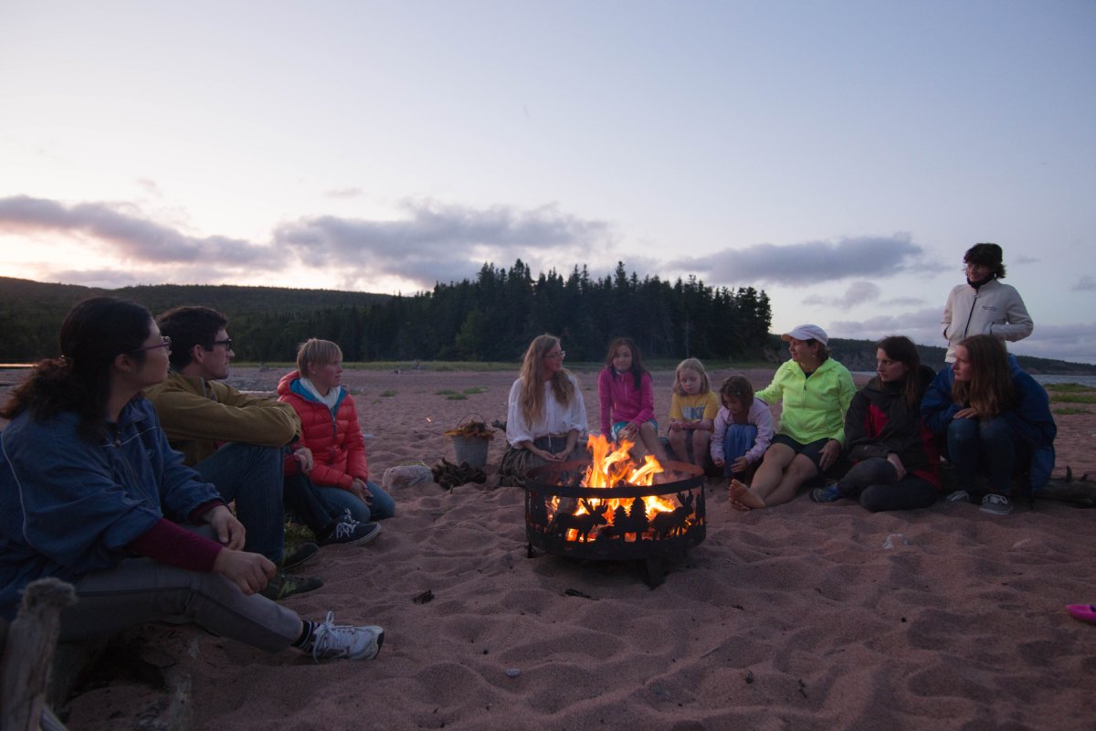 Un groupe de personnes assises autour d’un feu de camp sur une plage au crépuscule.