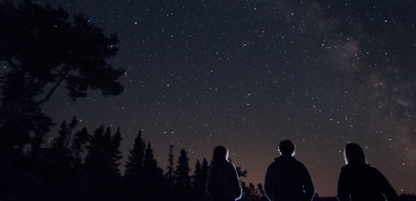 Trois personnes se tiennent ensemble et regardent le ciel nocturne rempli d'étoiles.