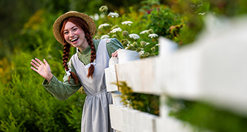Anne salue derrière une clôture blanche à Green Gables