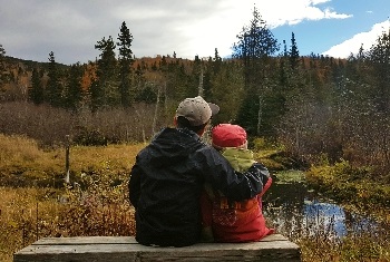Assis sur un banc, un jeune garçon entoure de son bras une petite fille devant un paysage d’automne