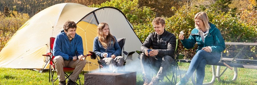 Quatre amis sont assis autour d'un foyer, l'automne, au camping Des-Rosiers. Derrière eux, une tente jaune et les montagnes colorées