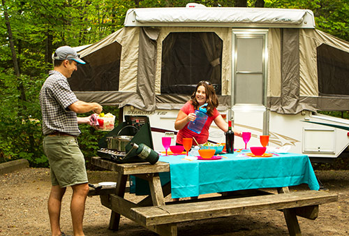 Un père et sa fille cuisinnent devant une tente-roulotte