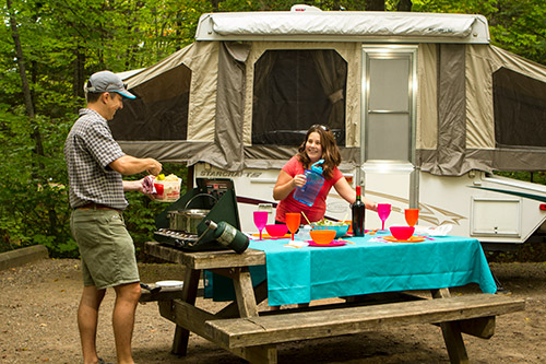 Un père et sa fille cuisinent devant une tente-roulotte