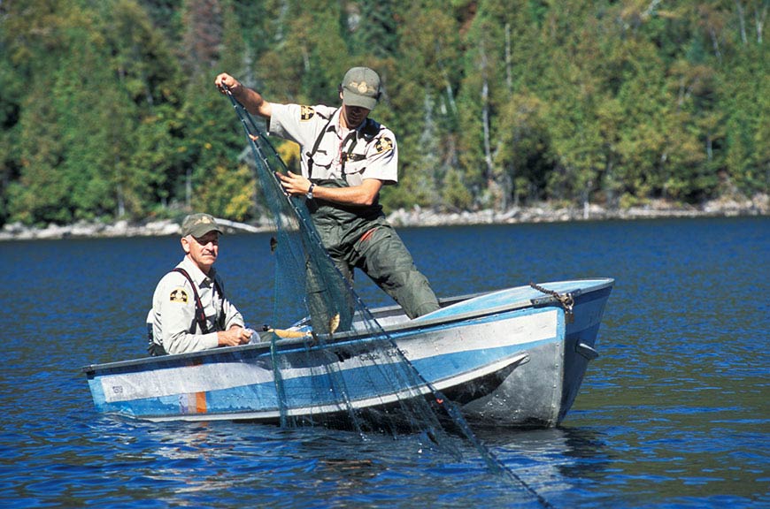 Un employé à bord d’une embarcation retire un filet de pêche de l’eau.