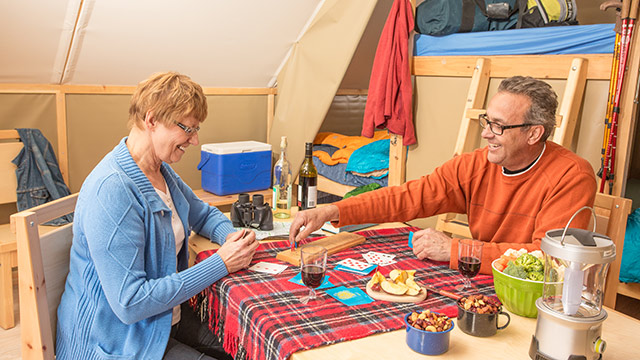 Un couple joue aux cartes et déguste une collation, tout en profitant du confort de la tente oTENTik de Parcs Canada, au parc national des Prairies. 