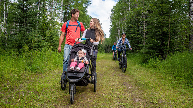 Un couple se promène avec son enfant dans une poussette sur les sentiers Red Deer et Fisher tandis que des visiteurs les croisent en bicyclette, au parc national de Prince Albert.