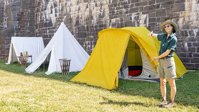 Une membre du personnel de Parcs Canada se tient à côté de deux tentes historiques et d’une tente moderne.