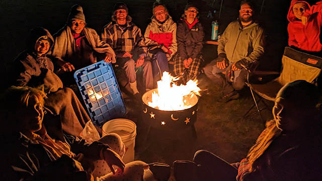 Un groupe est assis autour d’un feu de camp en soirée.