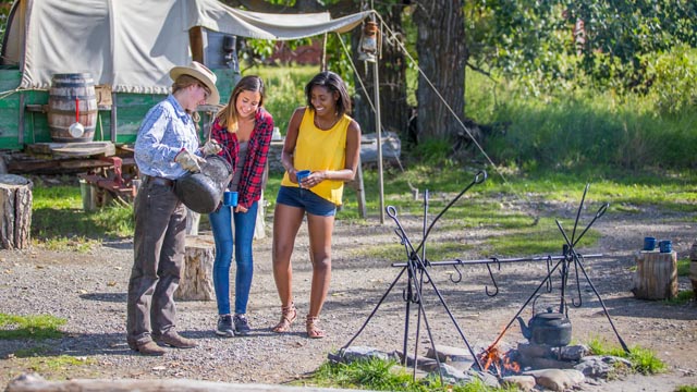 Un interprète de Parcs Canada offre un café des cowboys traditionnel à deux jeunes femmes au camp de rassemblement au lieu historique national du Ranch Bar U.