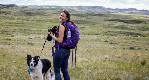 Une femme prend des photos dans les prairies lors d'une randonnée avec son chien.
