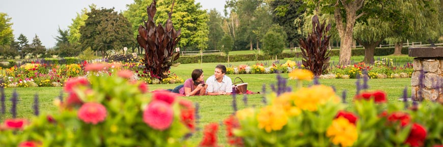 Deux visiteurs font un pique-nique dans les jardins victoriens colorés avec de vieux saules en arrière-plan.
