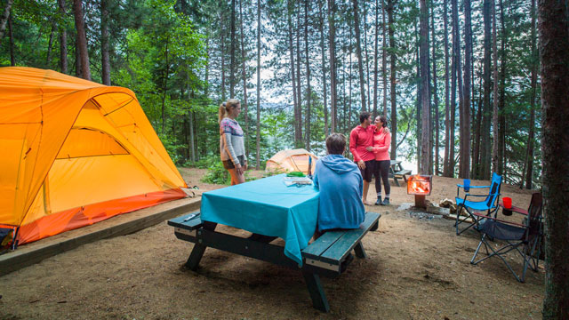 Un site de canot-camping en bordure du lac Wapizagonke avec quatre visiteurs près d’un feu, d’une table et d’une tente au parc national de la Mauricie.