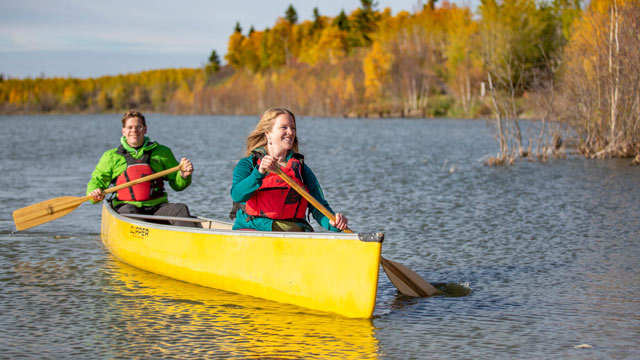 Deux jeunes adultes font du canot sur le lac Astotin à Elk Island par une journée d’automne ensoleillée.