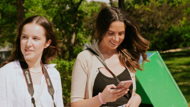 Deux jeunes femmes, dont une avec un téléphone, marchent dans un parc.
