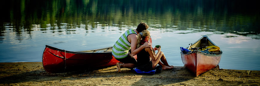Un couple est assis sur le bord du lac près de canots.